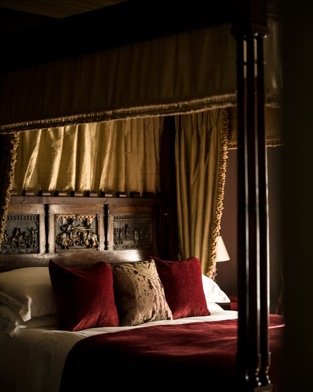 A sumptuous carved oak four poster bedhead, with red velvet cushions