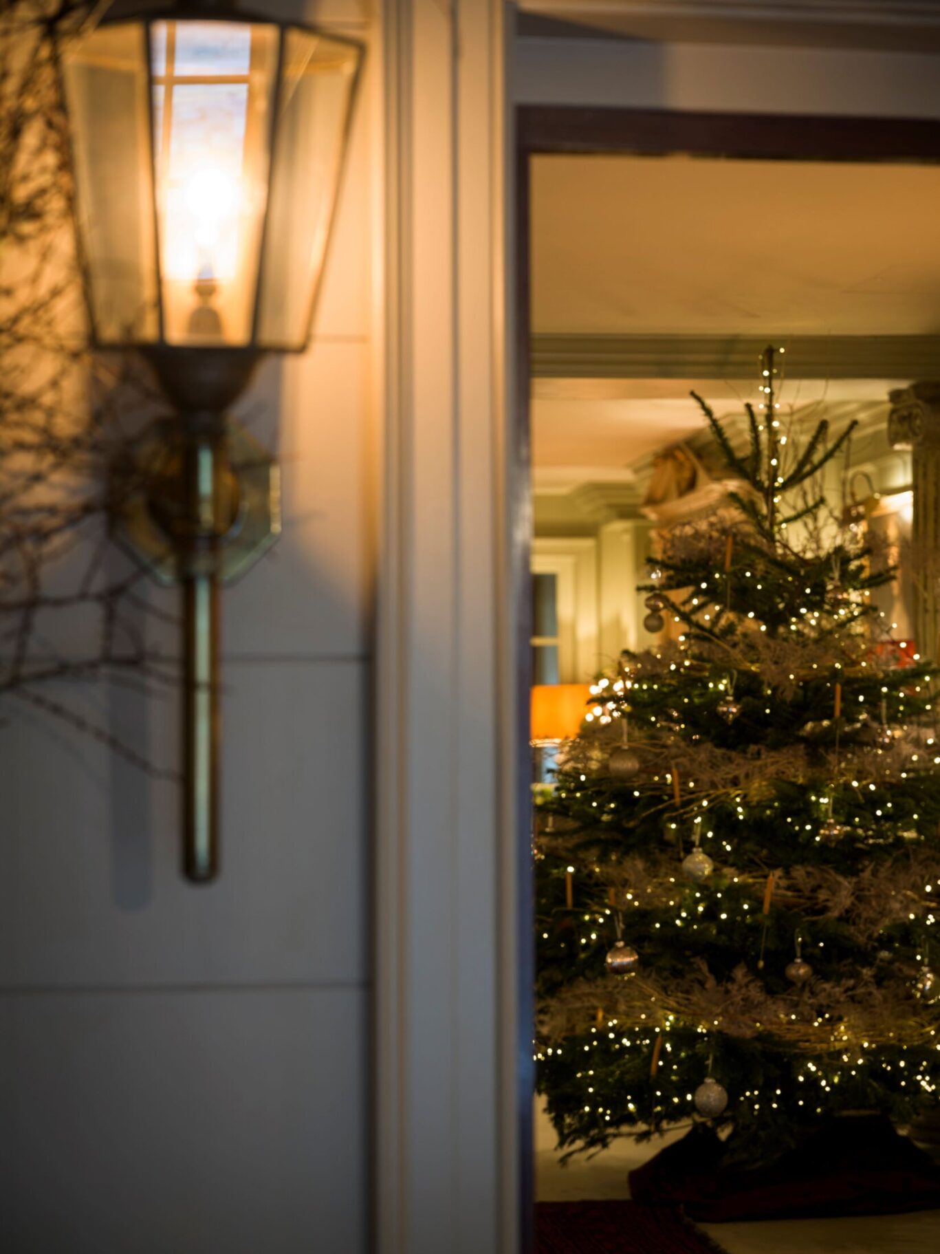 Warmly lit Christmas tree seen through the entrance of Batty Langley’s in Spitalfields, with an exterior lantern in the foreground.